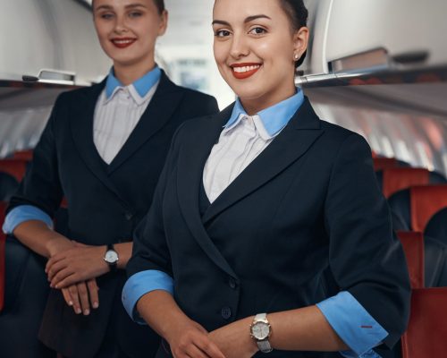 Two stewardesses standing on airplane aisle with folded hands
